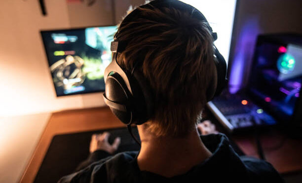 Rear View of Gamer with Headset on Playing Online Video Games in Dark Room